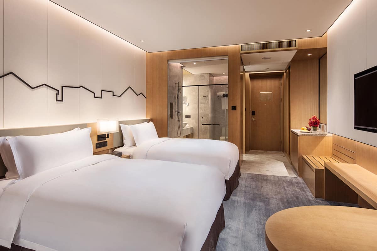 Een moderne hotelkamer met twee bedden, een bureau, een televisie en een douche.