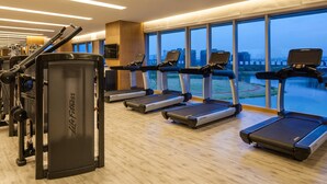 Un gimnasio con cintas de correr, máquinas de pesas y un amplio ventanal con vistas a la ciudad.