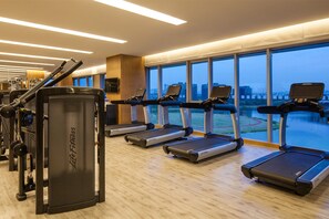 Un gimnasio con cintas de correr, máquinas de pesas y un amplio ventanal con vistas a la ciudad.