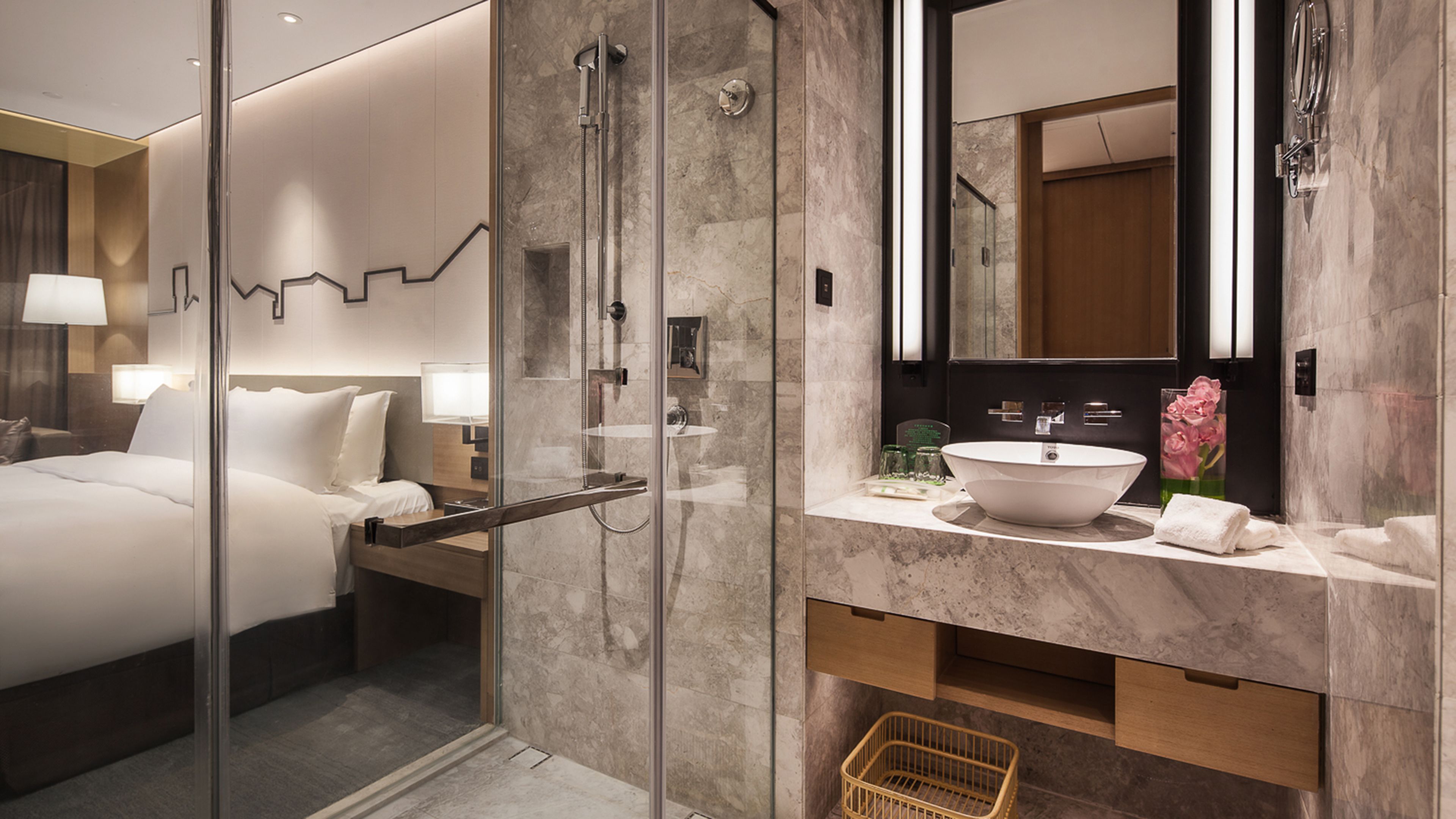 Een moderne hotelbadkamer met een douche met glazen wand, een grote spiegel en een marmeren aanrechtblad.