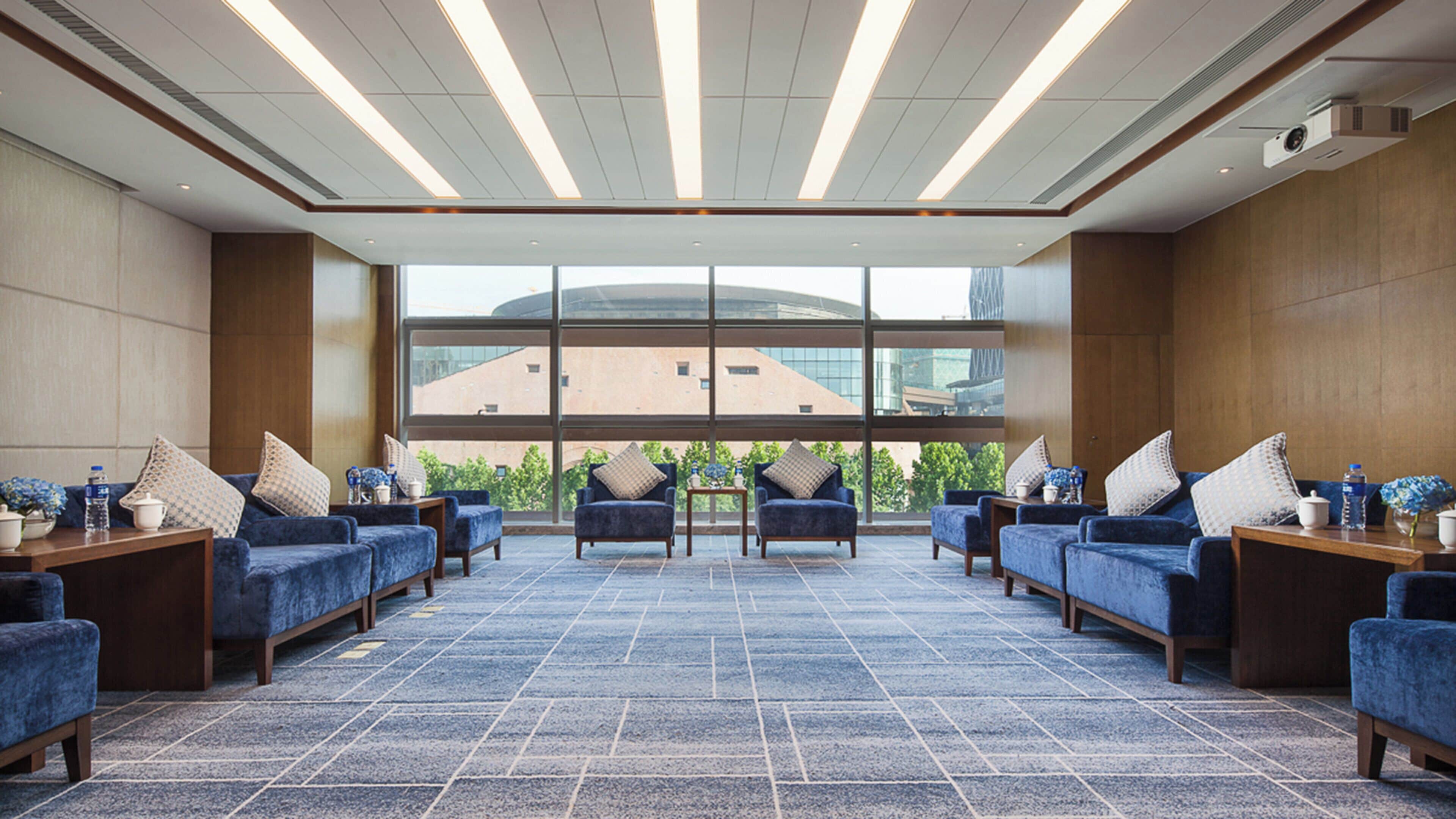 Una hall d'hotel dal design moderno, con un'area salotto con divani e poltrone, un'ampia finestra vista sulla città e un soffitto con illuminazione lineare.