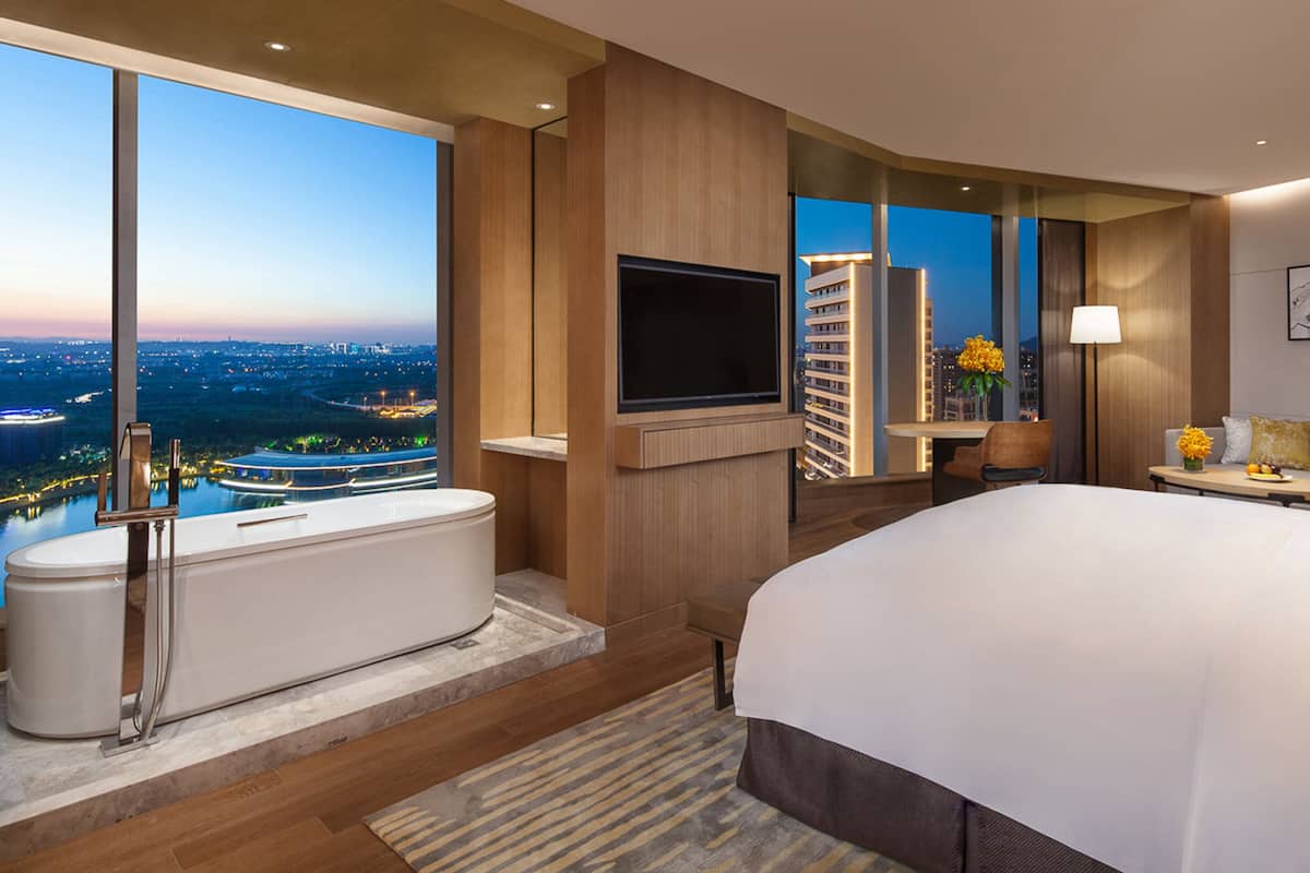 Een moderne hotelkamer met een groot bed, een badkuip, een flatscreen televisie en uitzicht over de stad.