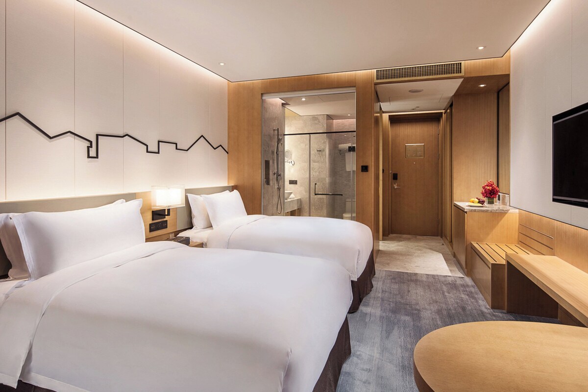 Una habitación de hotel moderna con dos camas, un escritorio, un televisor y una zona de ducha.