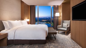 Ein Hotelzimmer mit einem großen Bett, einem Sessel, einem Fernseher und Blick auf eine Stadtlandschaft.