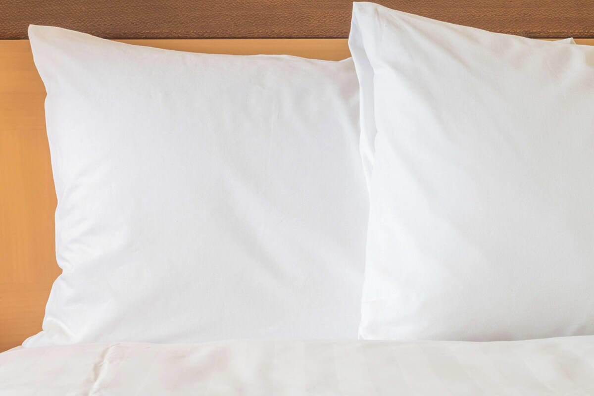Una cama con ropa blanca y almohadas frente a un cabecero marrón.