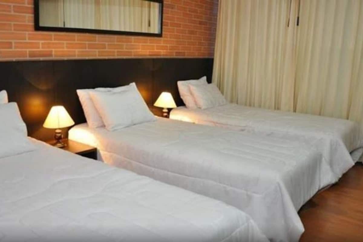 Habitación de hotel con dos camas, cada una con cabecera, lámparas de noche y pared de ladrillo detrás.