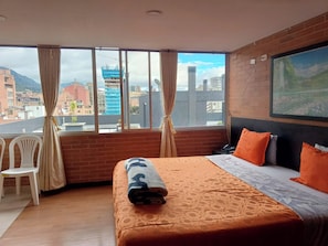 Une chambre d’hôtel avec un grand lit, une vue sur le paysage urbain, un mur en briques et une fenêtre avec des rideaux.