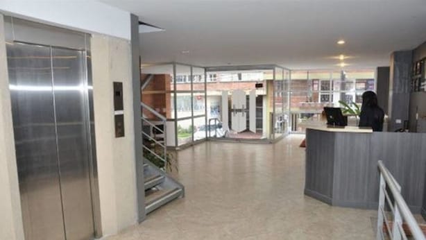 A modern hotel lobby with a reception desk, a staircase, and a glass elevator. - Hotel Bogota Astral (Bogotá)