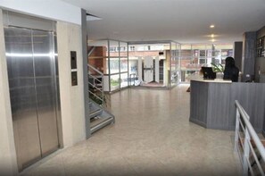En modern hotellobby med en receptionsdisk, en trappa och en glashiss.