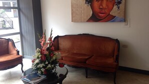 A living room with a brown sofa, a glass coffee table with books and flowers, and a large painting on the wall. - Hotel Bogota Astral (Bogotá)