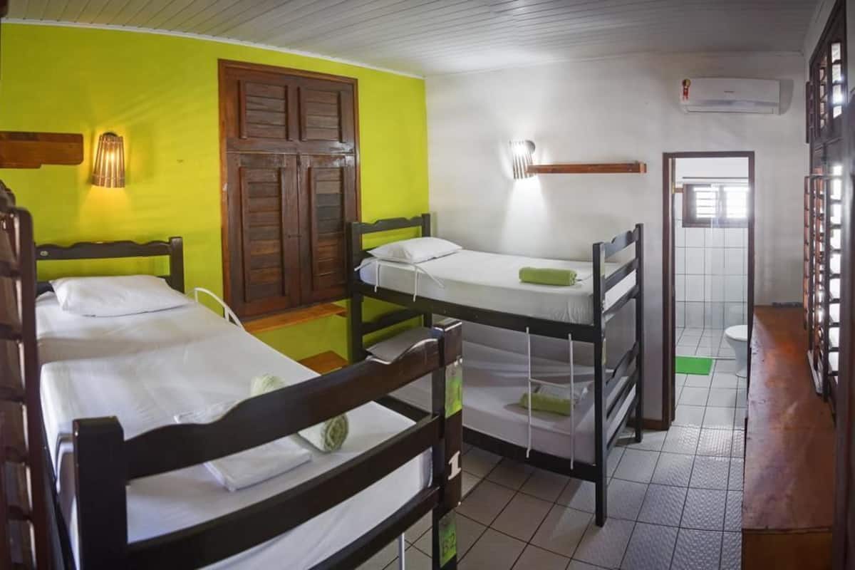 A dormitory room with two bunk beds, a wooden wardrobe, a wall-mounted lamp, and a window with a view.