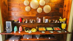 A buffet setup with various food items, a coffee machine, and a juice dispenser. - Mandala Hostel (Jijoca de Jericoacoara)