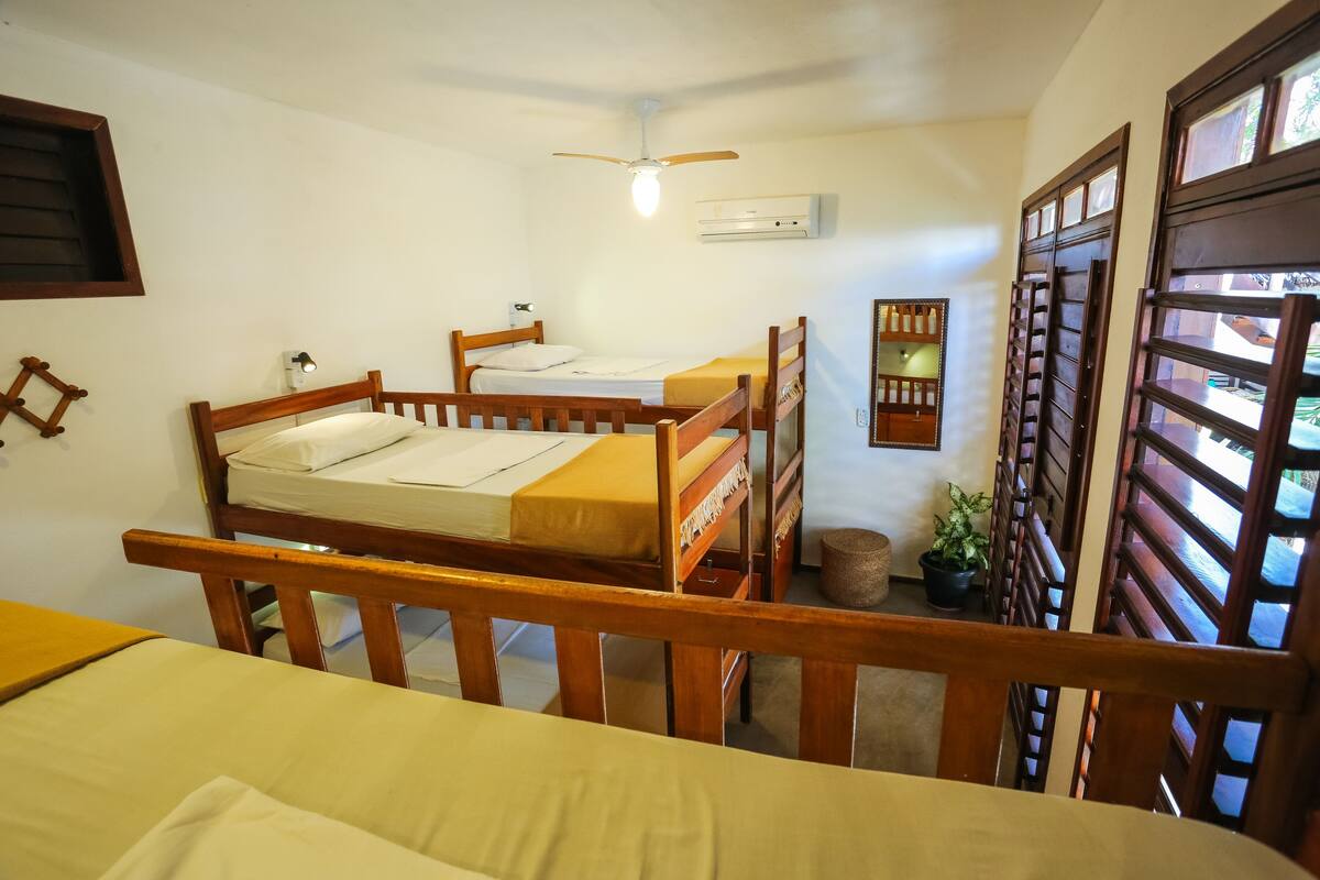 A dormitory room with bunk beds, a ceiling fan, an air conditioning unit, and a window with a view.