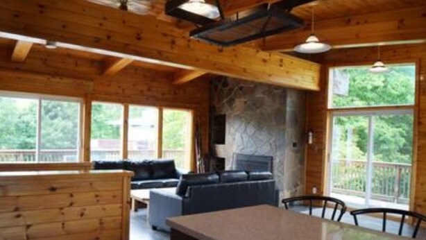 A cabin interior with a stone fireplace, wooden walls, a sofa, and a dining area. - 6 Bed Blue Mountain Chalet with Hot Tub 8 (The Blue Mountains)