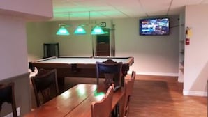 A pool table with green overhead lights, a television mounted on the wall, and a wooden table with chairs. - 6 Bed Blue Mountain Executive Chalet with Hot Tub 157 (The Blue Mountains)