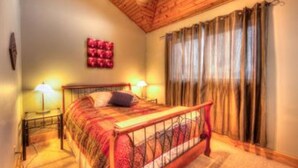 A bedroom with a wooden ceiling, a bed with a red and white bedspread, two bedside lamps, and a window with curtains. - 5 Bed Blue Mountain Luxury Chalet with Hot Tub 159 (The Blue Mountains)