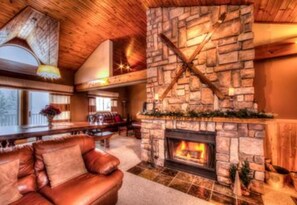 A cozy living room with a stone fireplace, leather sofa, and a wooden ceiling. - 5 Bed Blue Mountain Luxury Chalet with Hot Tub 159 (The Blue Mountains)