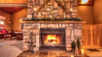 A stone fireplace with a fire, a wooden ceiling, and a red couch in the background.
