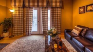A cozy living room with a leather sofa, a coffee table with a bottle and glasses, plaid curtains, and a potted plant. - 5 Bed Blue Mountain Luxury Chalet with Hot Tub 159 (The Blue Mountains)