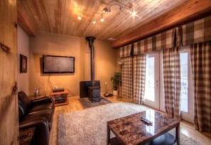 A cozy living room with a fireplace, a sofa, a coffee table, and plaid curtains. - 5 Bed Blue Mountain Luxury Chalet with Hot Tub 159 (The Blue Mountains)