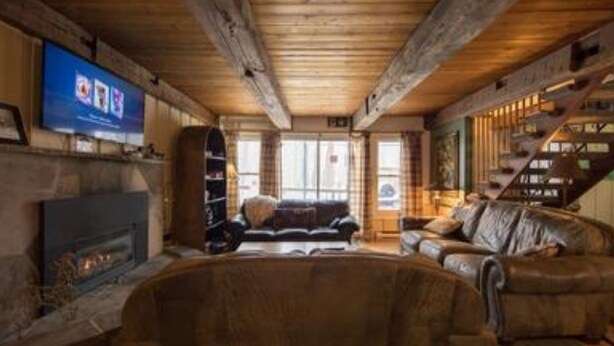 Una sala de estar acogedora con chimenea, sofás de cuero y una televisión montada en la pared.