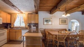 Una cocina rústica con armarios de madera, una mesa de comedor con sillas y un amplio ventanal con cortinas.