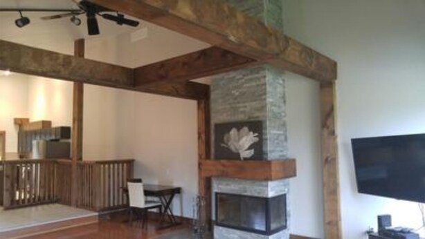 A spacious living room with exposed wooden beams, a stone fireplace, and a flat-screen TV mounted on the wall. - 7 Bed Blue Mountain Tyrolean Chalet with Hot Tub 35L (The Blue Mountains)