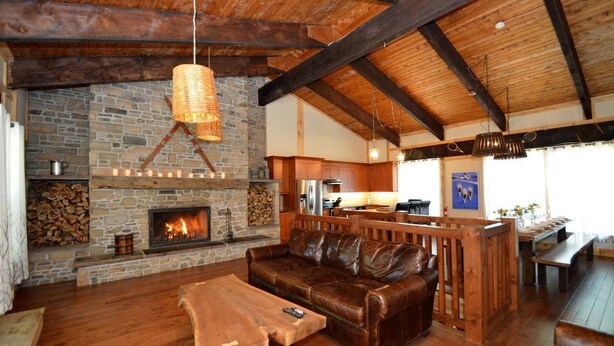 A cozy interior with a stone fireplace, wooden beams, a leather sofa, and a rustic dining area.