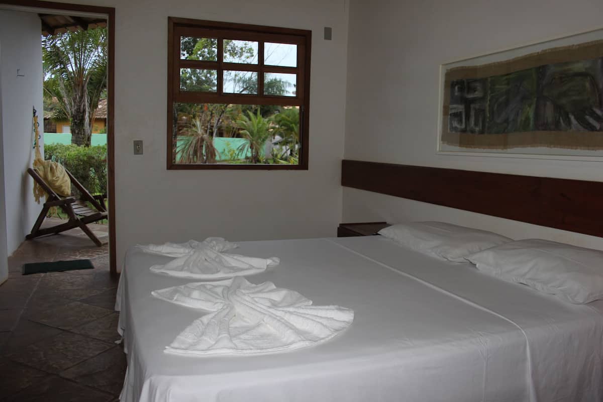 A hotel room with a large bed, a window with a view of palm trees, and a painting on the wall.