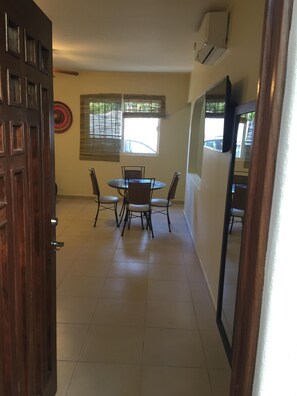 A dining area with a round table and four chairs, a window with blinds, and a door with a decorative panel.