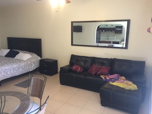 Un dormitorio con una cama, un sofá, una mesita y una silla. Hay un espejo en la pared y un ventilador de techo.
