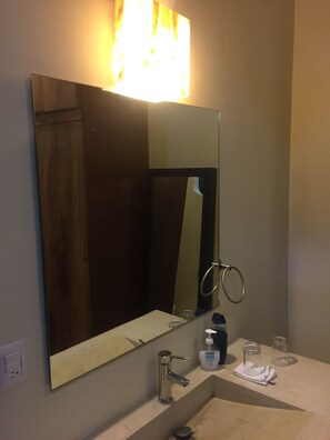 A bathroom with a large mirror, a sink, a towel, a soap dispenser, and a glass.