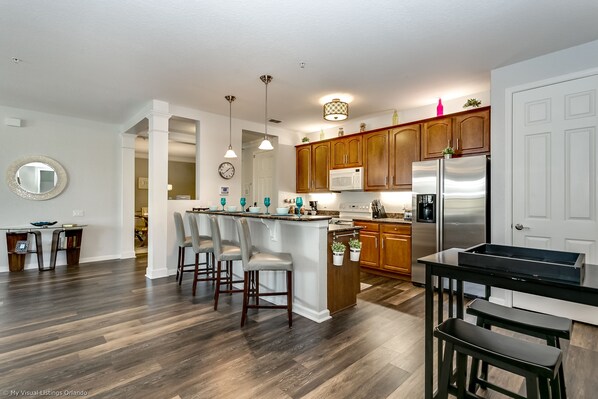 A modern kitchen with wooden cabinets, stainless steel appliances, and a central island with bar stools. - Work from home while you relax at this Safe & Clean home Miranda’s Gem (Orlando)