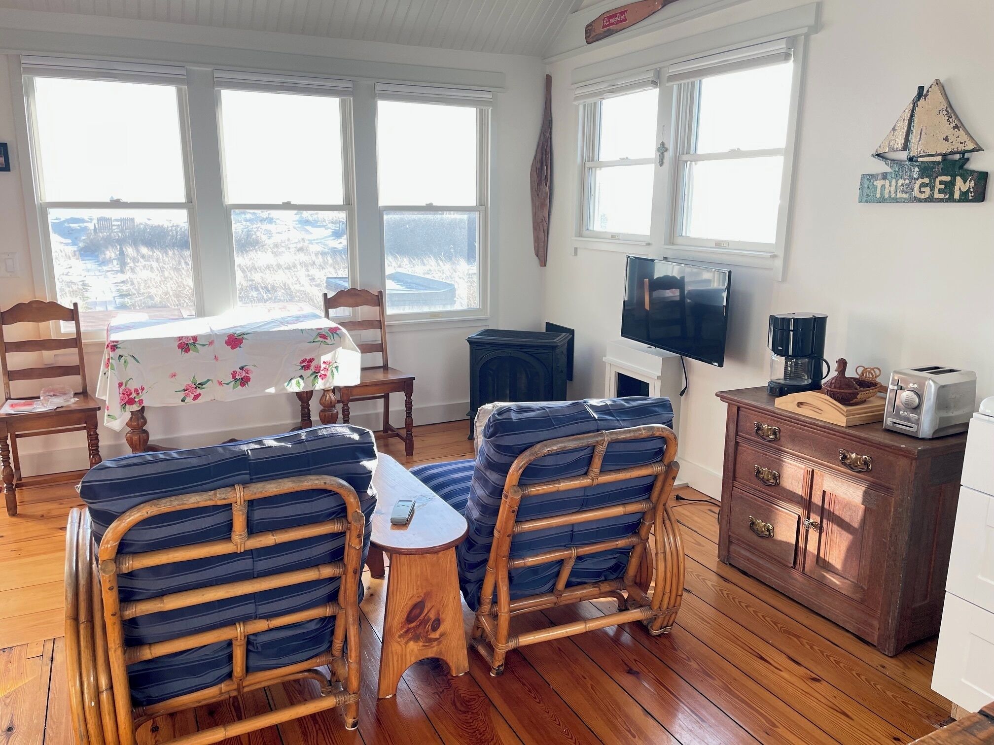 A cozy room with a wooden floor, a dining table with chairs, a television, a coffee maker, and a dresser.