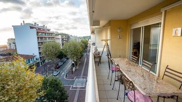 Un balcón con mesa y sillas de mármol, que da a una calle con árboles y edificios.