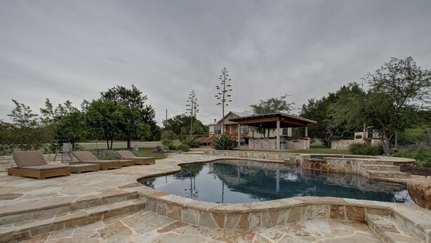 A stone pool with steps leading into it, surrounded by lounge chairs and a wooden deck.