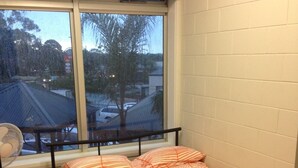 A single bed with a striped blanket in a room with a window overlooking a parking area and trees. - McLaren Vale Backpackers (McLaren Vale)