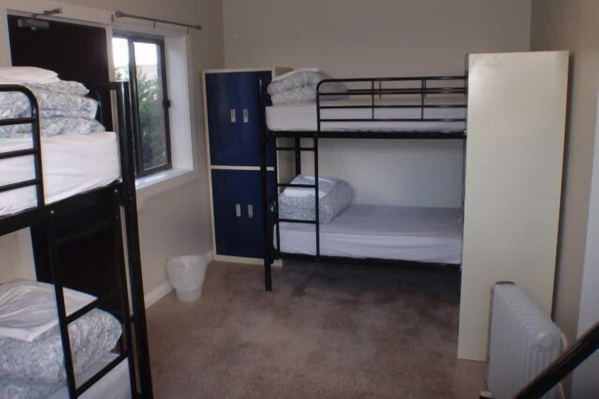 A dormitory room with bunk beds, a radiator, and a window.
