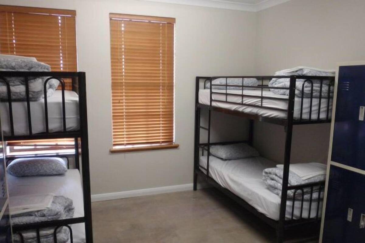 A dormitory room with bunk beds, a window with blinds, and a blue locker.