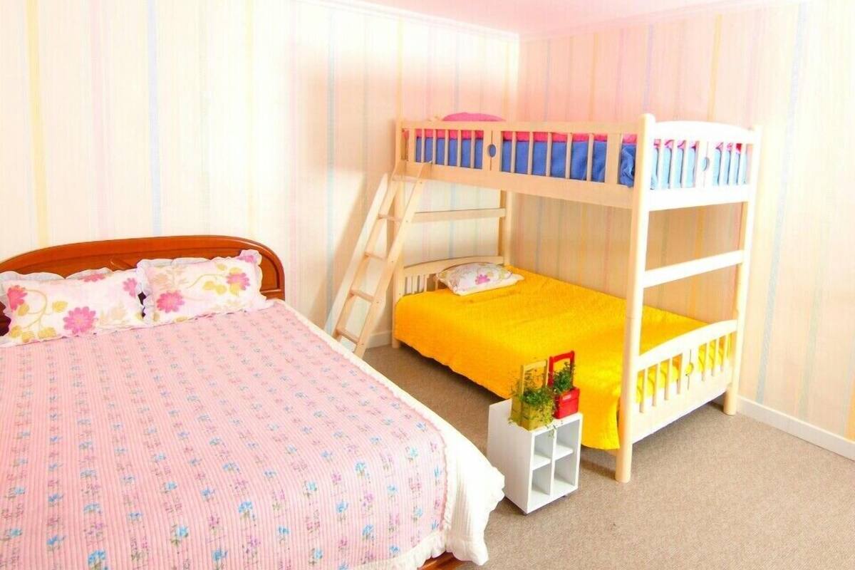 A child's bedroom with a bunk bed, a single bed, and a small white shelf.