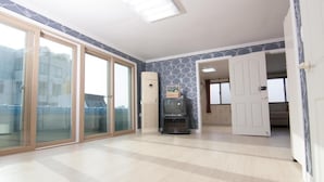 Una habitación amplia con un gran ventanal corredero que da a un espacio exterior, un equipo de aire acondicionado integrado y un televisor sobre un mueble.