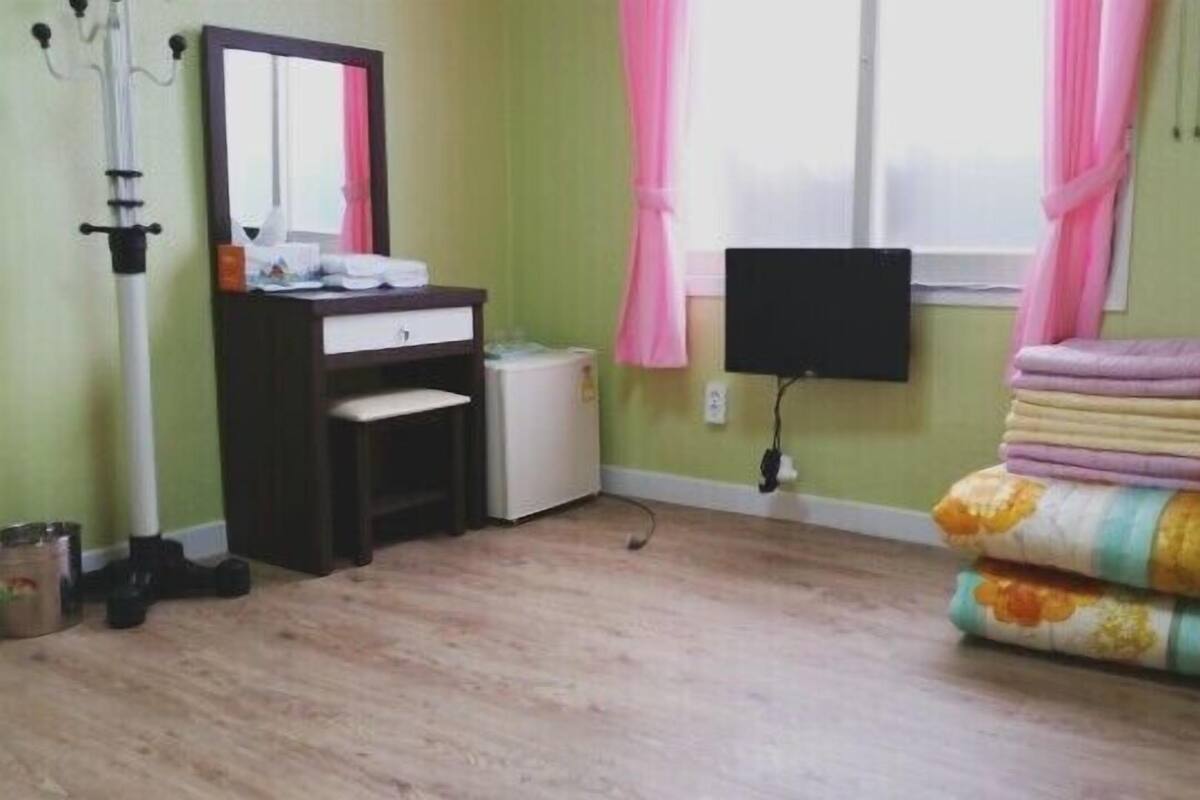 A room with a bed, a dresser, a mirror, a TV, and a window with curtains.
