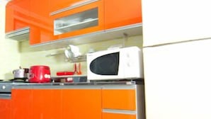 Una cocina con armarios color naranja, un microondas blanco y una tetera roja.
