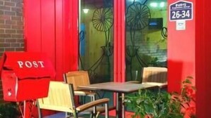Un edificio rojo con un letrero de oficina postal, un banco y un ventanal con un diseño floral.