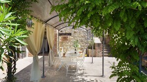 Un patio al aire libre con un muro de piedra, una mesa con sillas y una botella de vino.