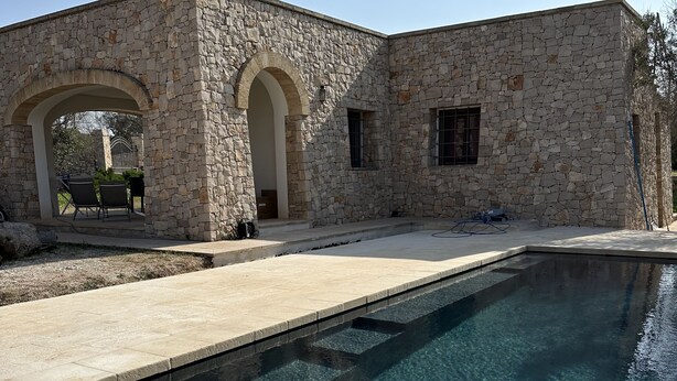 Um edifício de pedra com piscina, área de estar ao ar livre e céu limpo.