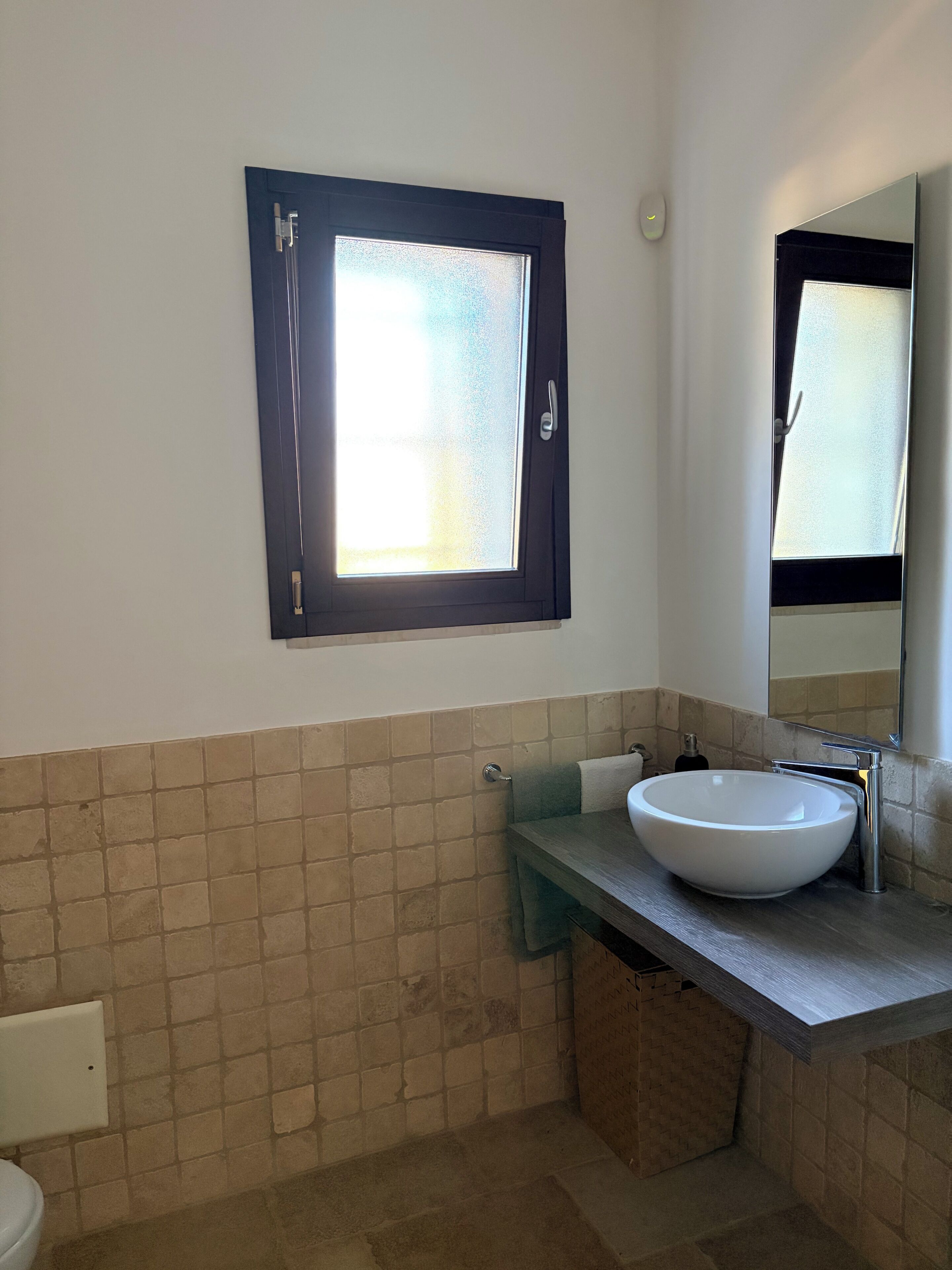 A bathroom with a white sink, a towel rack, a window with frosted glass, and a mirror.