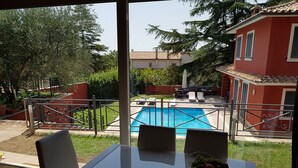 A dining area with a table and chairs, a pool in the background, and a red building with a tiled roof. - Detached house with large private pool for exclusive use (Riano, Roma)