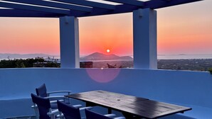 A terrace with a table and chairs, overlooking a sunset with a mountain in the distance. - Spacious, private luxury villa with pool, & stunning sea and sunset views (Glinado)