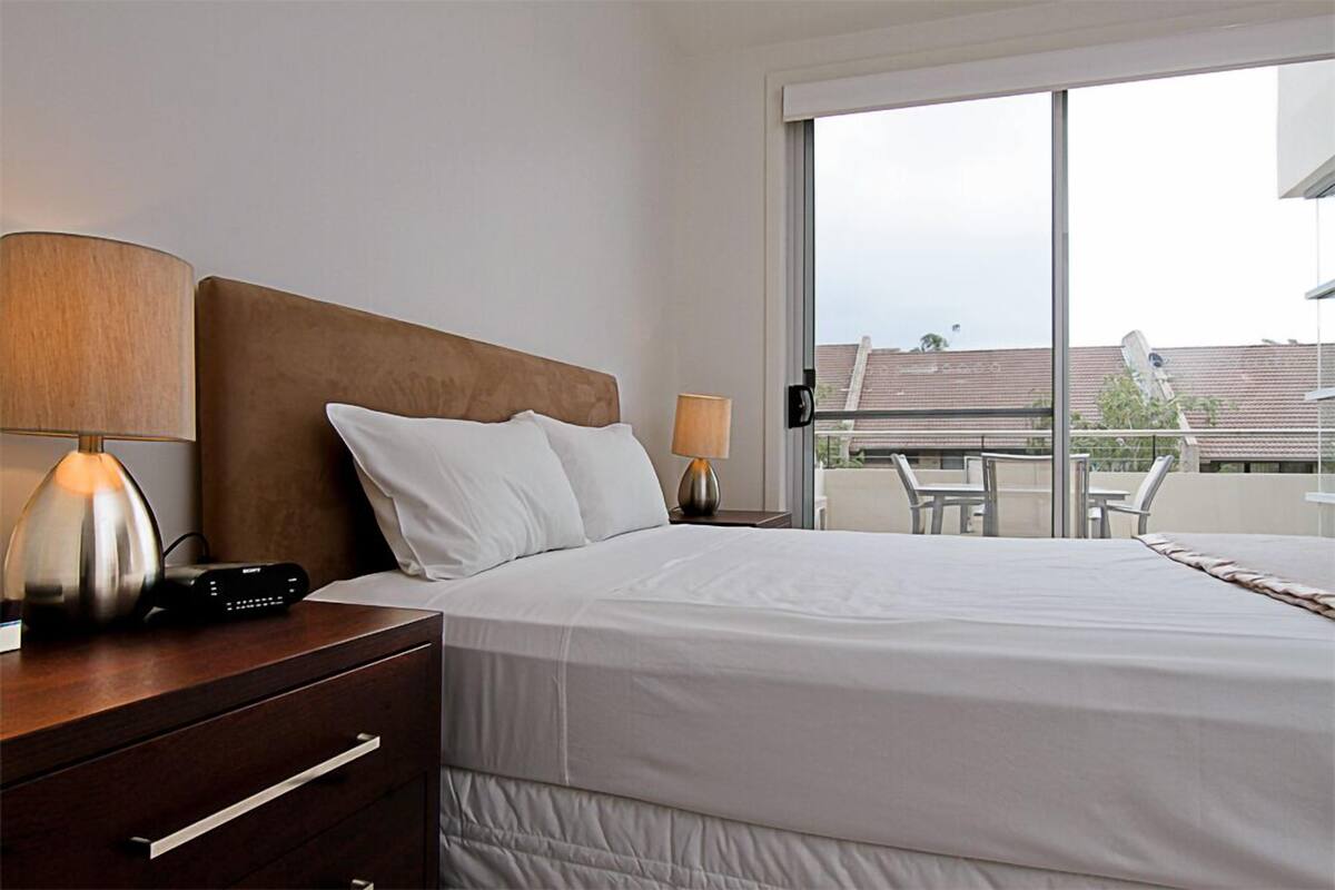 Une chambre d’hôtel avec un lit, des tables de chevet, des lampes et une vue sur le balcon extérieur.
